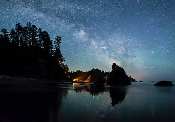 The Milky Way lights up the southern sky while a campfire illuminated the seas stacks on Ruby Beach in Olympic National Park, Washington.