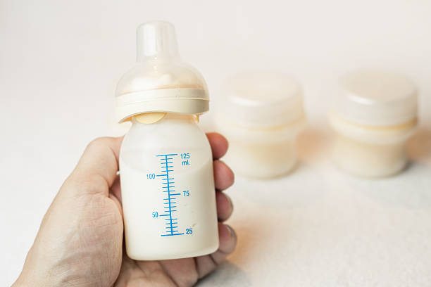 istock Father holding a baby bottle with breast milk with scale 481447616