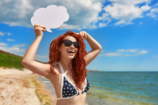 laughing red hair woman holding empty space cloud idea above her head and smiling, wearing swimwear, summer season.