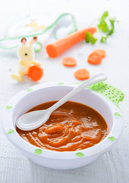 Carrot puree for baby nutrition in plate on green tablecloth