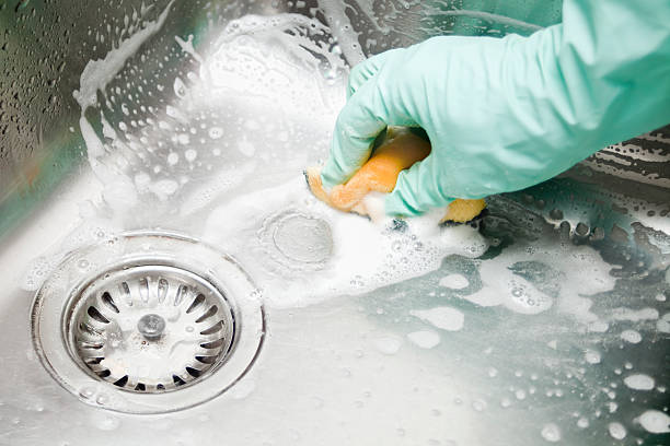 Scrubbing the kitchen sink. Human hands with protective gloves scrubbing up a square shaped large kitchen sink with a scouring pad, soap bubbles . cleaning sponge photos stock pictures, royalty-free photos & images