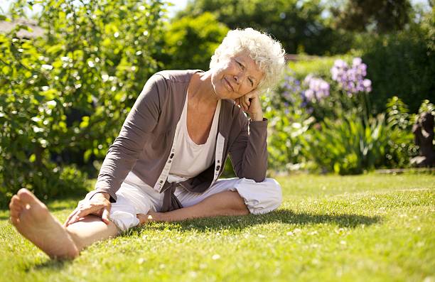 reife frau sitzt auf gras komfortabel - formal garden flower bed women grass stock-fotos und bilder