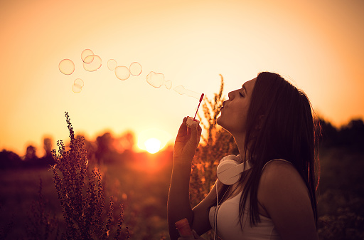 Young woman blowing bubbles in field at sunset