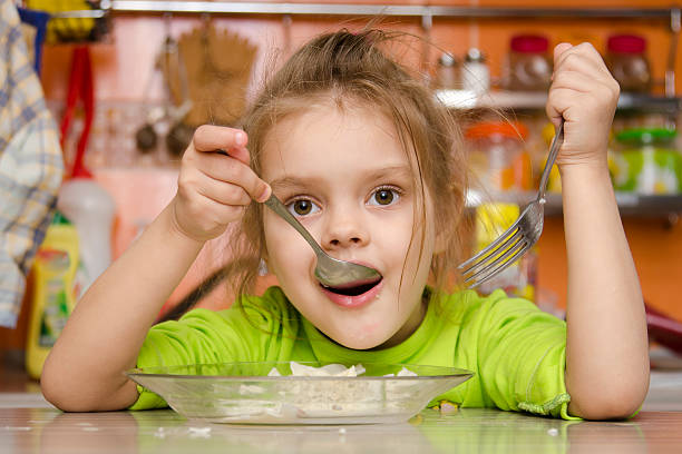 istock girl eats with fork and spoon sitting in kitchen 481470173
