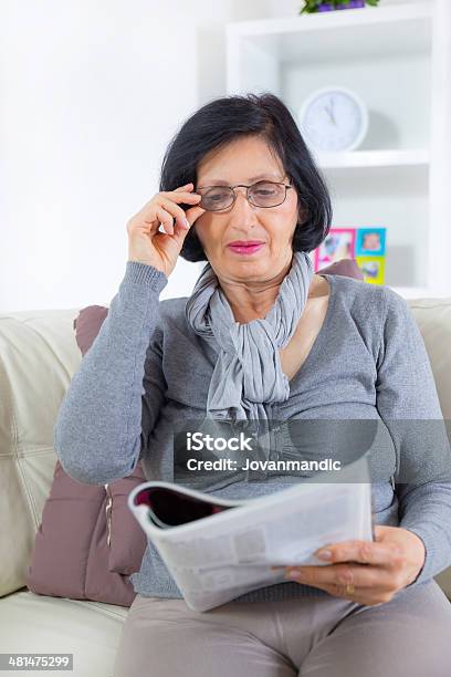 Mature Woman Reading Magazine At Home Stock Photo - Download Image Now - Looking Away, Women, Eyeglasses