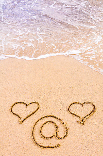 istock Two hearts  and at sign drawn in the sand 481484025