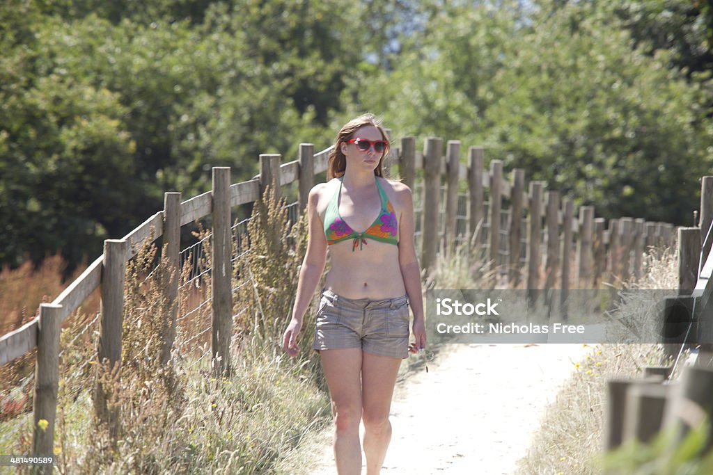 Summertime Stroll young woman surfer taking a stroll to the along the path to the beach Adult Stock Photo