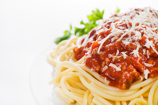 Freshly grated parmesan cheese falls on a plate of spaghetti and meatballs.
