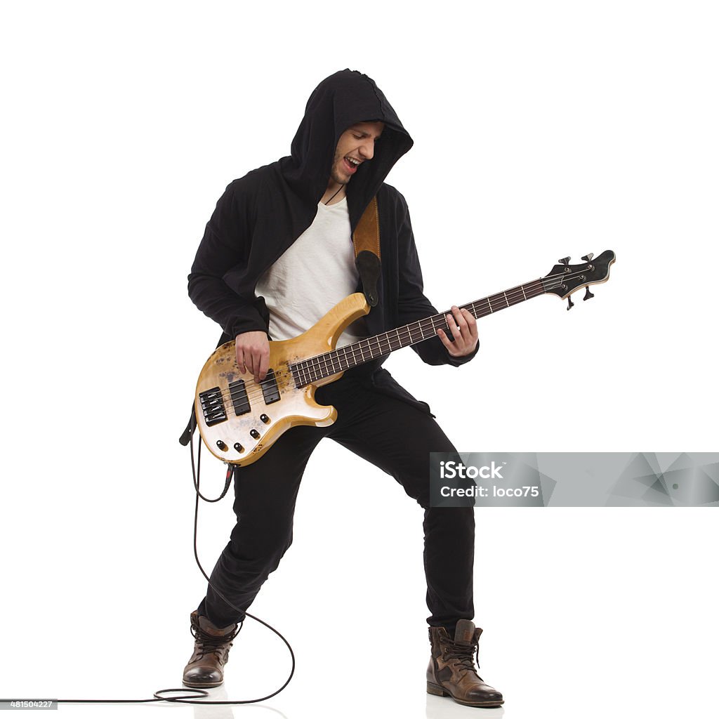 Male guitarist with bass guitar. Shouting guitarist in black hoodie play the bass guitar. Full length studio shot isolated on white. Bass Guitar Stock Photo