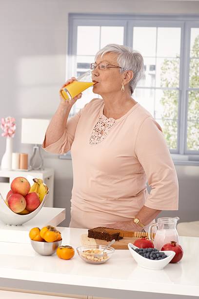 Mulher idosos beber sumo de laranja - fotografia de stock