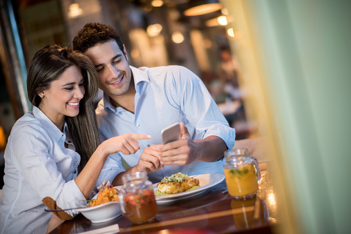 Couple having dinner at a restaurant and looking at a mobile phone while smiling
