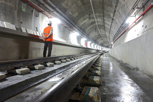 Underground metro tunnel. An engineer is staring at the level of rails looking towards the end of line. 