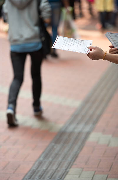 Flyer Hand-out Female hand is offering a flyer to people passing on the street. In the small print on the flyer is a lunch menu. No restaurant name visible passing giving stock pictures, royalty-free photos & images