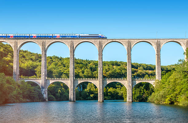 French TGV train on stone viaduct in Rhone-Alpes France Cize, France - July 9, 2015: French high speed train TGV operated by SNCF, national rail operator on Cize-Bolozon viaduct bridge in Ain, Rhone-Alpes region in France. This train was developed during the 1970s by GEC-Alsthom and SNCF. A TGV test train set the record for the fastest wheeled train, reaching 574.8 km/h (357.2 mph) on 3 April 2007. Viaduct of Cize-Bolozon in summer season in Bugey along Ain river. This viaduct is a combination rail and vehicular viaduct crossing the Ain gorge. An original span built in the same location in 1875 was destroyed in World War II. Reconstructed as an urgent post-war project due to its position on a main line to Paris, the new viaduct reopened in May 1950. It carries road and rail traffic at different levels. passenger train photos stock pictures, royalty-free photos & images