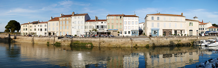St. Martin-De-Re, France - June 25, 2015: Boats in harbour at St Martin-De-Re. People, shops and restauarants are in the background surrounding the quayside. Stitched panorama