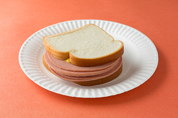 Large bologna sandwich with mustard A several slices of bologna sandwich with mustard and white bread on a paper plate atop an orange table top. baloney stock pictures, royalty-free photos & images