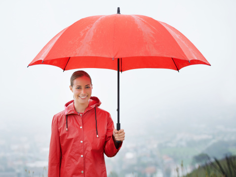 A beautiful young woman standing outside while holding her red umbrella