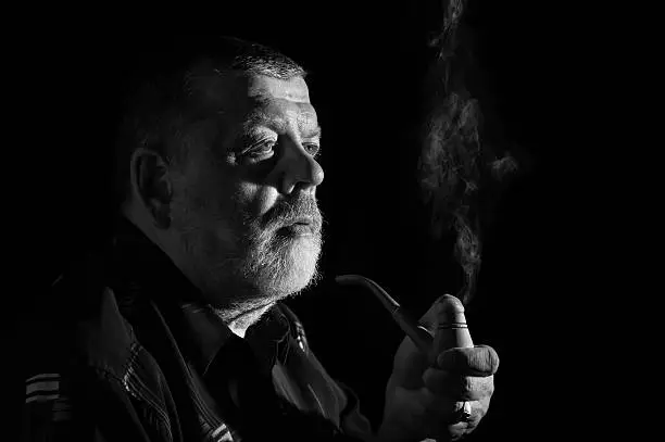 Black and white dramatic portrait of senior smoking tobacco pipe