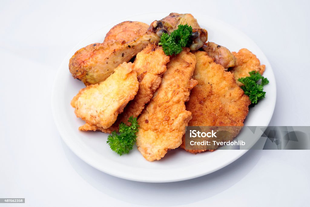 Breaded pork chops and chicken legs on plate Restaurant food of tasty roasted breaded pork chops and chicken legs with golden crust decorated with parsley on plate isolated on white, horizontal picture 2015 Stock Photo