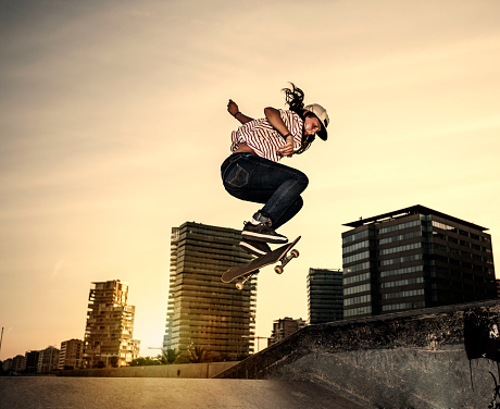 Female teenager skateboarder jumping in skateboard park at sunset