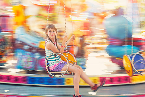 Happy little girl aged 9 havig fun on swing carousel. Panning shot. The girl is slightly soft, background is motion blurred. The girl is smiling into the camera.