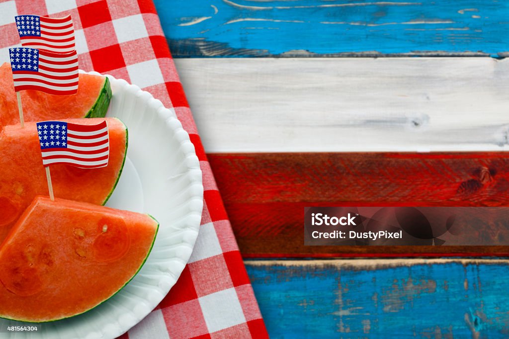 Patriotic Picnic with US Flags in Watermelon Slices US flags in plated slices of watermelon on a red, white and blue picnic table with red checked table cloth for patriotic holiday picnics such as July Fourth, Memorial Day and Labor Day. American Flag Stock Photo