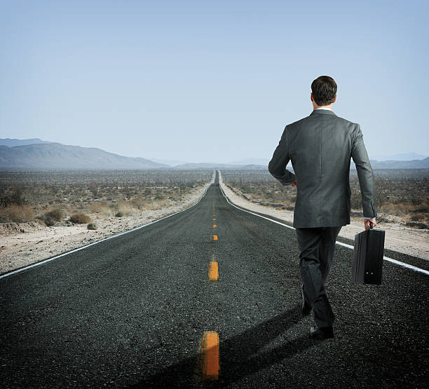istock Businessman holding briefcase walking down long desert highway 481566669