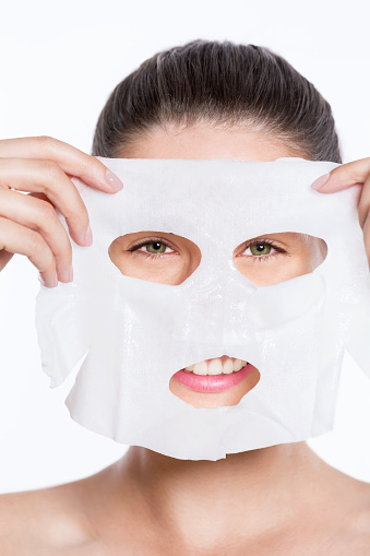 Beautiful young woman puttingcloth facial mask on her face