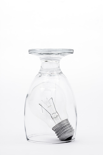 An upside down drinking glass confining a lightbulb on a white background.