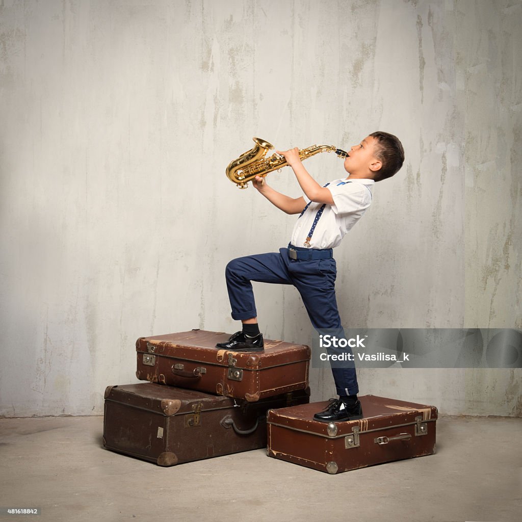 Seis años viejo niño de pie con las maletas y jugar sax - Foto de stock de Niño libre de derechos