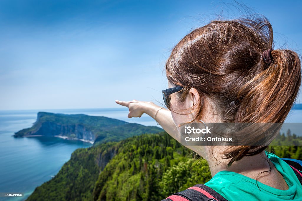 Woman on Mountain Summit Pointing a Direction Woman hiker wearing a backpack on a Mountain Summit and Pointing a Direction and the ocean. She is pointing the Gaspé Peninsula in Forillon, Quebec, Canada. 2015 Stock Photo