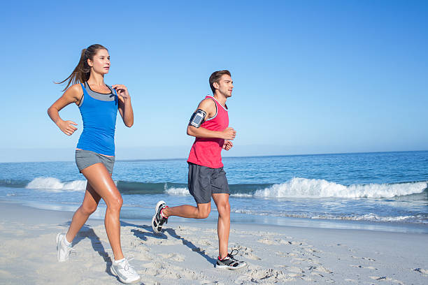 Group running on beach jogging having fun training. Exercising runners training outdoors living healthy active lifestyle. Multiracial fitness runner people working out together outside