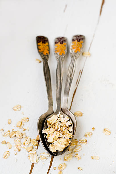 istock Three tablespoons of oatmeal lying on a white wooden background. 481643622