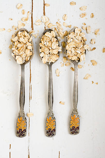 istock Three tablespoons of oatmeal lying on a white wooden background. 481643630