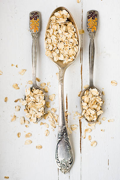 istock Three tablespoons of oatmeal lying on a white wooden background. 481643636