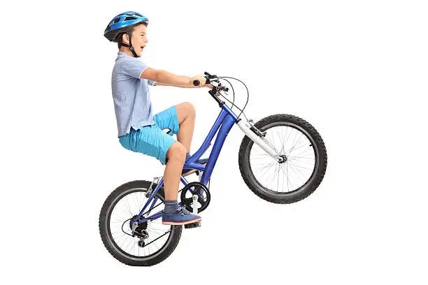 Profile shot of a little boy with blue helmet doing a wheelie on a small blue bike isolated on white background