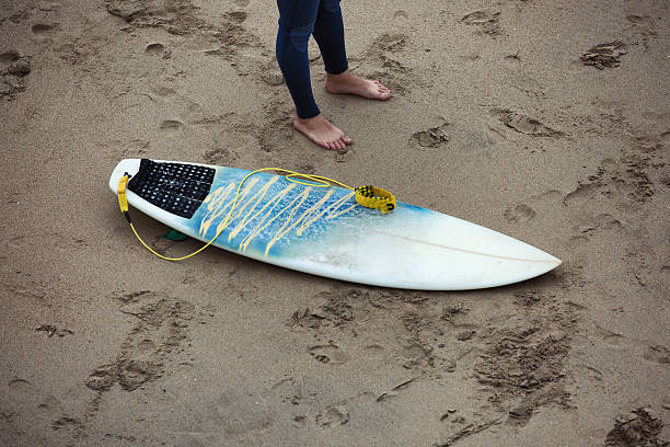 istock Surfboard on the beach next to the surfer legs. 481653908