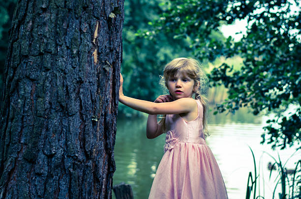 little blond girl with long hair leaned to the tree trunk