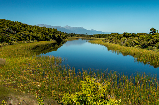 Small lake north of Haast, Sourth Island, New Zealand. The lake is immediately adjacent ot the ocean. Mountain range of Mount Aspiring National Park in the distance.