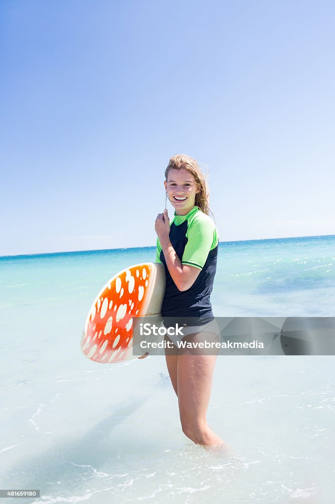 Fit blonde woman standing in the water and holding surfboard Fit blonde woman standing in the water and holding surfboard at the beach 18-19 Years Stock Photo