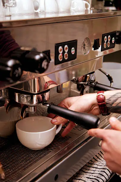 Close up of the hands of a barista preparing fresh coffee with an espresso machine.