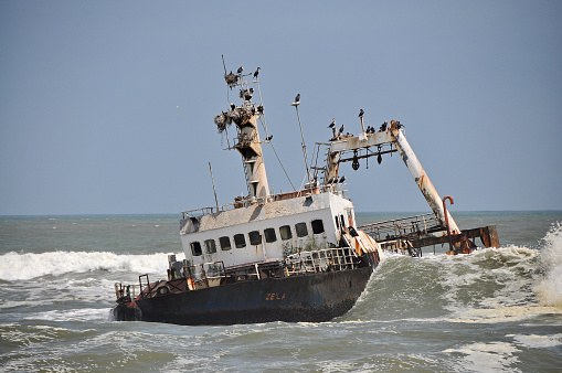 Wreck on the beach in Namibia. The waves roll to the ship. Birds have nests made in the masts of the wreck. The wreck lies in a blue sea deserted.