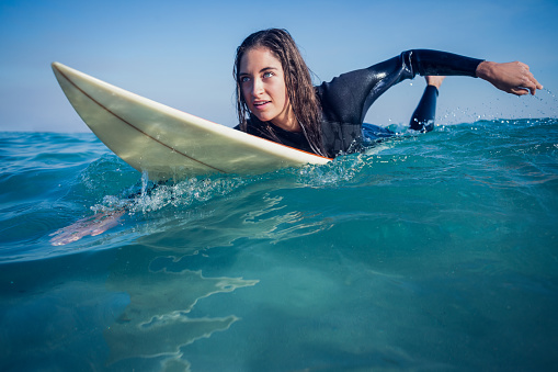 woman in wetsuit with a surfboard on a sunny day at the beach