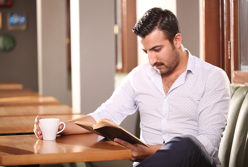 Middle eastern young man reading a book in cafe