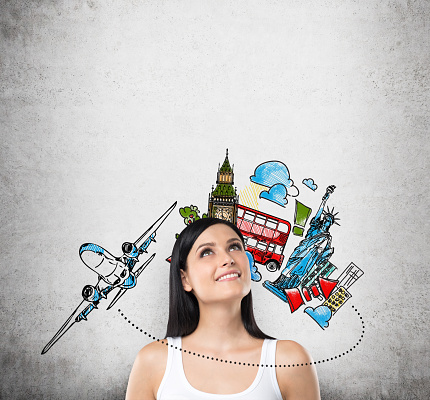 A portrait of a dreamy brunette lady in a white tank top. A concept of travelling and holidays. Colourful travelling sketch on the concrete wall.