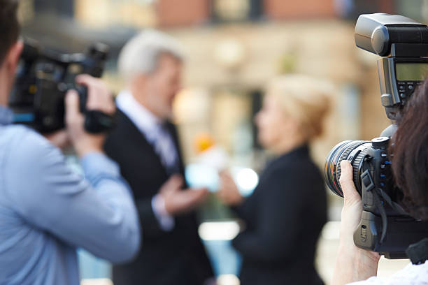 Photographer Taking Pictures Of Female Journalist Interviewing B Photographer Taking Pictures Of Female Journalist Interviewing Businessman announce stock pictures, royalty-free photos & images