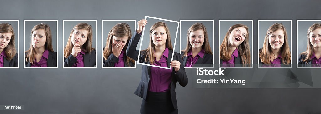 Business Woman with Various Personality, Character and Emotional Expressions Concept photo for personality, character and emotional expression. A woman in business suit holding up a photo of herself in front of her with various range of emotional expressions exhibited in the background wall behind her. From happiness to sadness, anger to joy, apprehension to confidence. Photographed in panoramic horizontal format in studio. Emotion Stock Photo