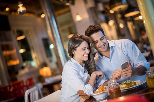 couple dans un restaurant regardant un téléphone portable - restaurant dinner dining gourmet photos et images de collection