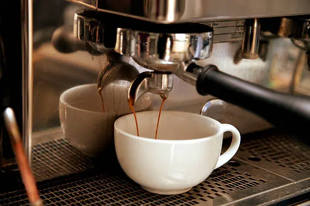 Close up of an espresso machine pouring fresh coffee into a white china cup.