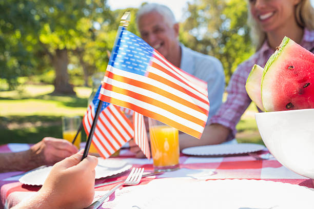 feliz familia tener picnic y sosteniendo bandera estadounidense - fourth of july family flag american flag fotografías e imágenes de stock